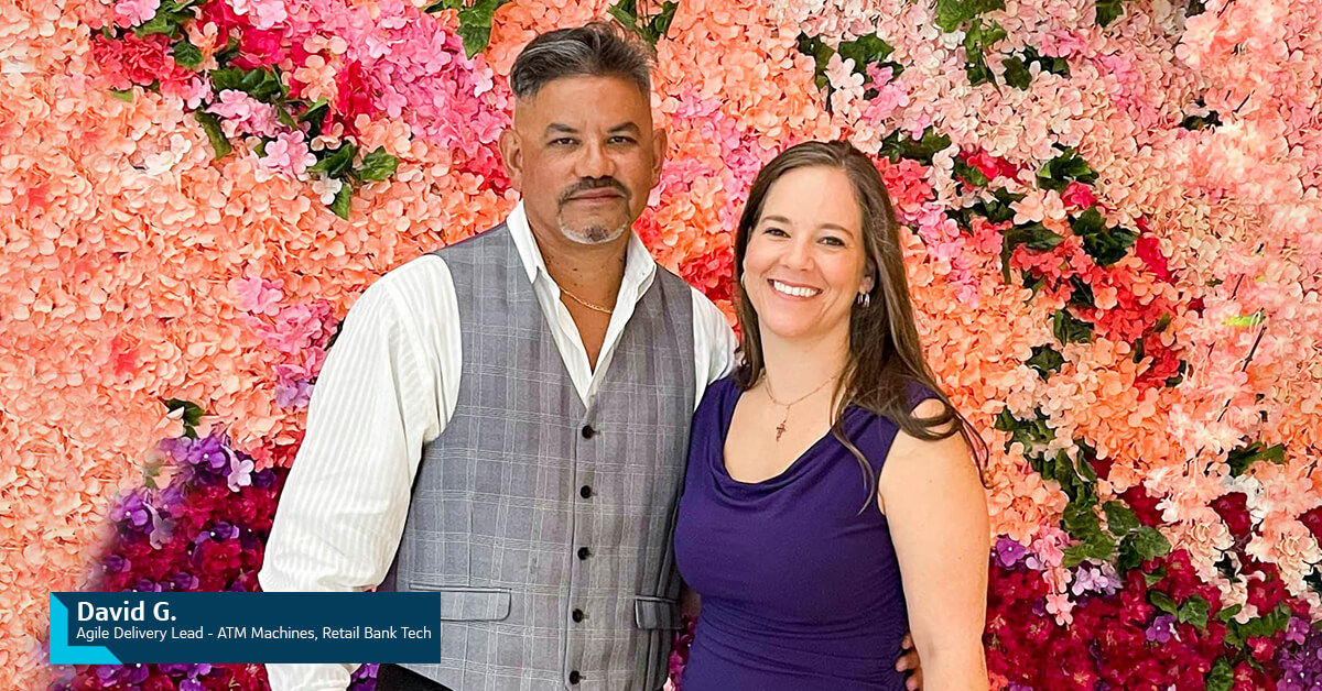 Capital One Veteran associate David G., Agile Delivery Lead - ATM Machines, Retail Direct Bank, Stands with his wife in front of a wall of pink flowers